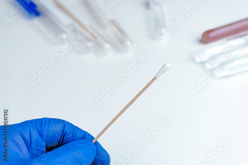 HAND HOLDING STERILE COTTON SWAB FOR CORONAVIRUS PCR TEST IN HOSPITAL LABORATORY.