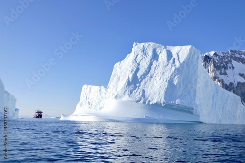 Cruise ship between icebergs in antarctic ocean, blue sky, sun, Antarctica