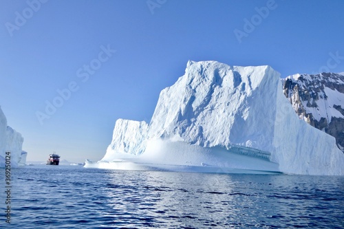 Cruise ship between icebergs in antarctic ocean, blue sky, sun, Antarctica