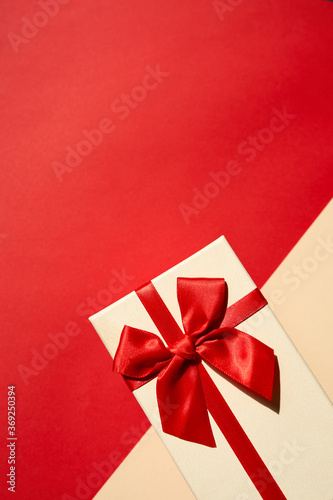Golden present with red ribbon on the bright red background . Festive backdrop for holidays: Birthday, Valentines day, Christmas, New Year.