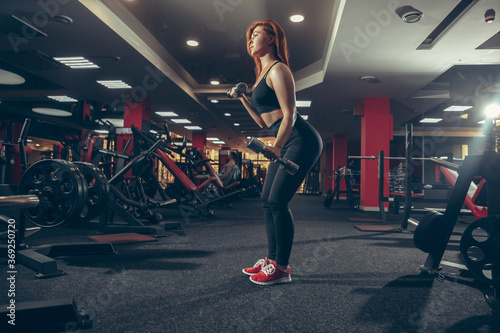 Concentrate. Young muscular caucasian woman practicing in gym with equipment. Athletic female model exercising, training her lower body, working out with weights. Wellness, healthy lifestyle