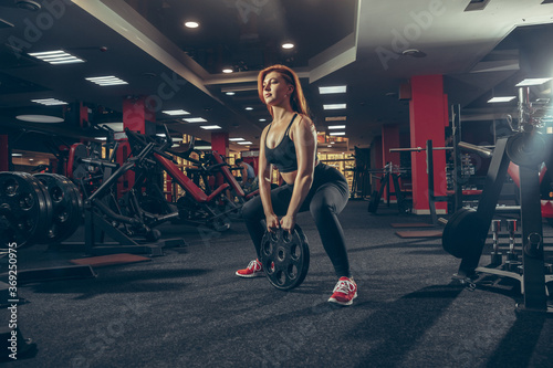 Concentrate. Young muscular caucasian woman practicing in gym with equipment. Athletic female model exercising, training her lower body, working out with weights. Wellness, healthy lifestyle