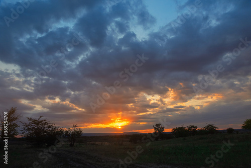 sky with thick blue clouds with bright orange evening sun over the field