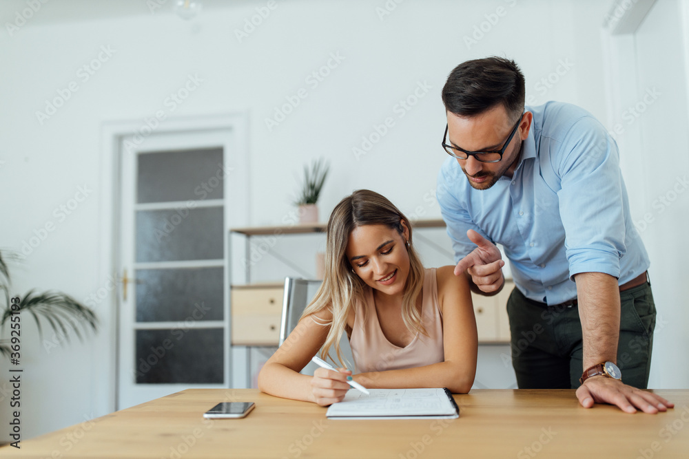 Couple of people discussing ideas over paper notebook at bright office. Couple of people discussing ideas over paper notebook at bright office.