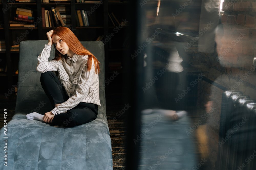 Attractive depressed red-haired young woman patient sitting on comfortable armchair and telling about her problems to psychotherapist. . Concept of psychological treatment.