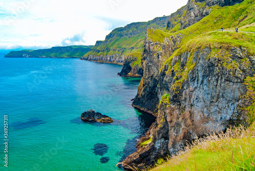 Antrim Coast near Carrick-a-Rede rope bridge in Northern Ireland. Blue sea and green lush vegetation on rocks. 
