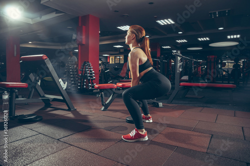 Sit up. Young muscular caucasian woman practicing in gym with equipment. Athletic female model exercising, training her lower body, working out with weight. Wellness, healthy lifestyle, bodybuilding.