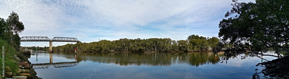 Beautiful panoramic view of a river with reflections of a tall pedestrian and water pipe  bridge, trees, deep blue sky and puffy clouds on water, Parramatta river, Rydalmere, Sydney, New South Wales, 