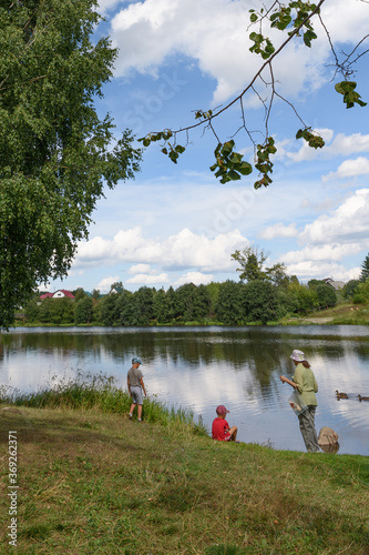 Fotografie On a summer day, a grandmother and her two grandsons rest on the riverbank