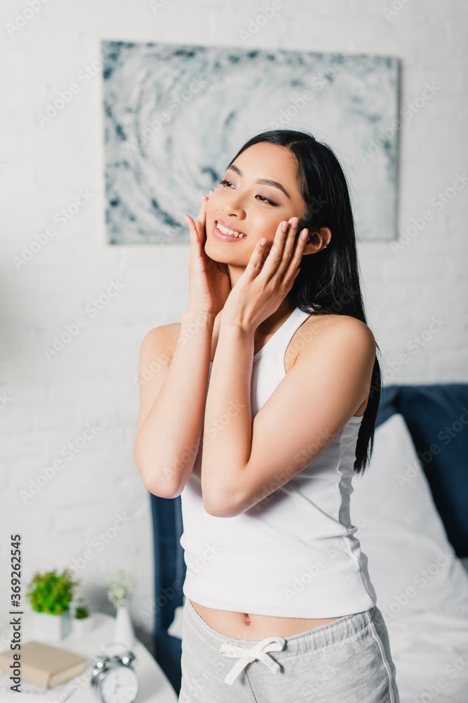 Beautiful asian woman smiling while touching face at home Beautiful asian woman smiling while touching face at home
