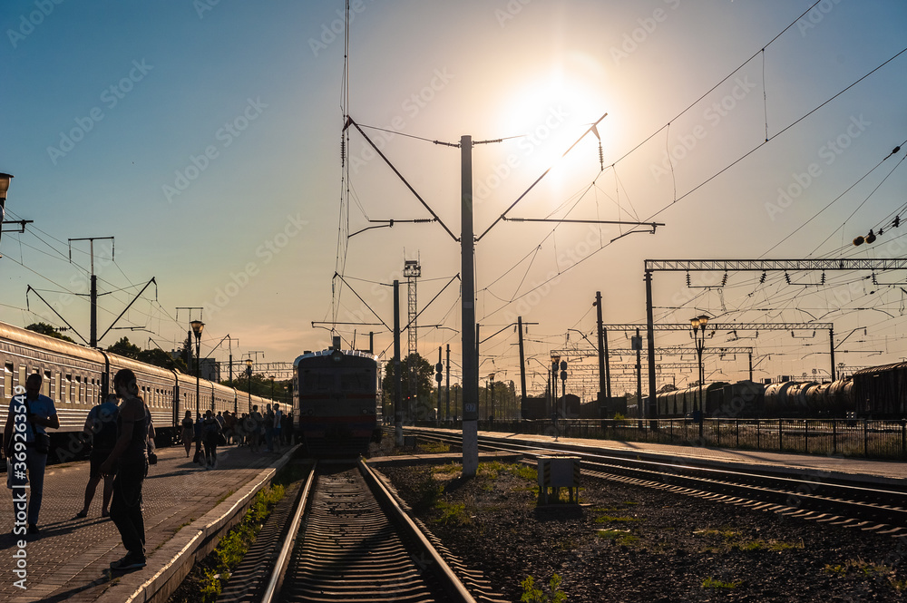 an old electric train drives up to the station platform along the rails at sunset