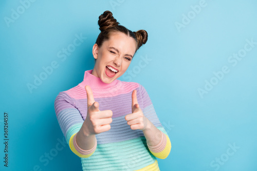Hey you. Photo of attractive crazy funky lady two buns directing fingers on camera blinking eye flirty person pick select wear casual warm striped sweater isolated blue color background photo
