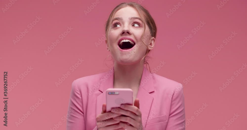  Shocked Girl  screaming Wow, Yes while using new Apps on Smartphone standing in  Isolated Studio in the Pink background