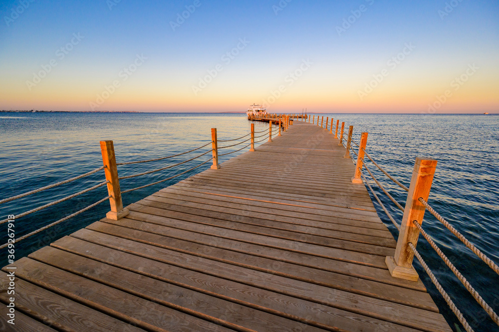 Fototapeta premium Wooden Pier on Red Sea in Hurghada at sunset and luxury yacht, View of the promenade boardwalk - Egypt, Africa