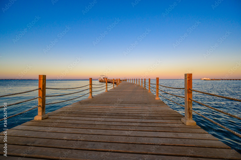 Fototapeta premium Wooden Pier on Red Sea in Hurghada at sunset and luxury yacht, View of the promenade boardwalk - Egypt, Africa