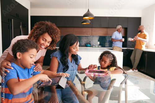 Grandmother With Mother Helping Grandchildren To Use Digital Tablets On Table At Home