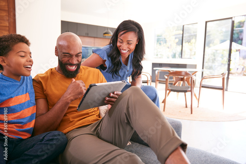African American Family With Son Sitting On Sofa At Home Using Digital Tablet