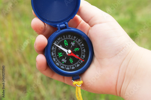 Old classic navigation compass in hand on natural background as symbol of tourism with compass, travel with compass and outdoor activities with compass