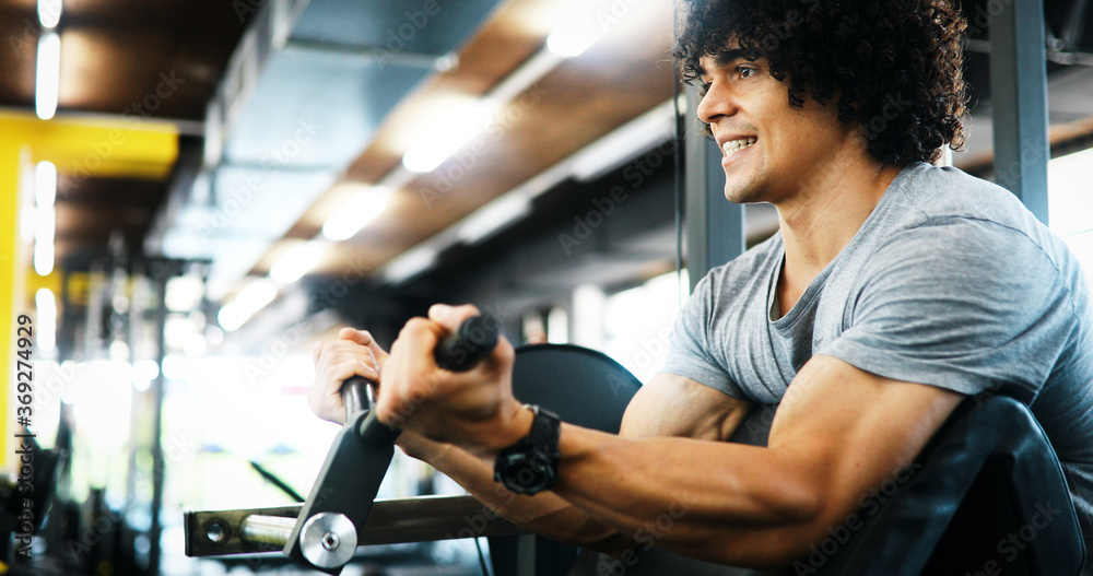 Muscular man working out in gym doing exercises with dumbbells at biceps