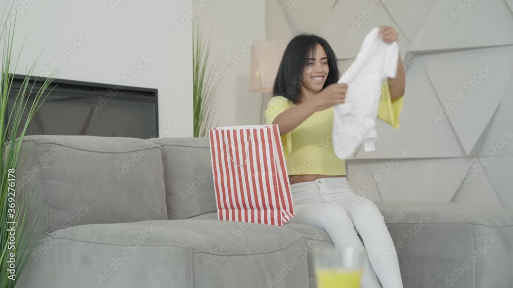 Happy African American woman entering room with shopping bag as son passing by at the background. Portrait of carefree female shopper enjoying purchase at home. Shopaholism concept. Happy African American woman entering room with shopping bag as son passing by at the background. Portrait of carefree female shopper enjoying purchase at home. Shopaholism concept.