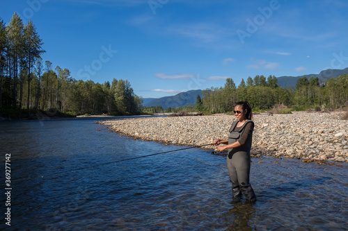 An asian women in waders, enjoying fishing a river in British Columbia, Canada