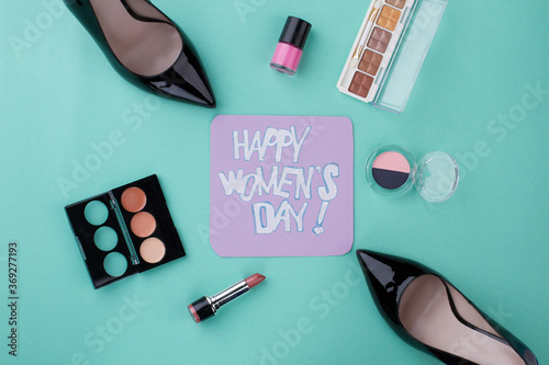 Happy women's day writing and beauty accesories. Top view flat lay. Isolated on turquoise background.