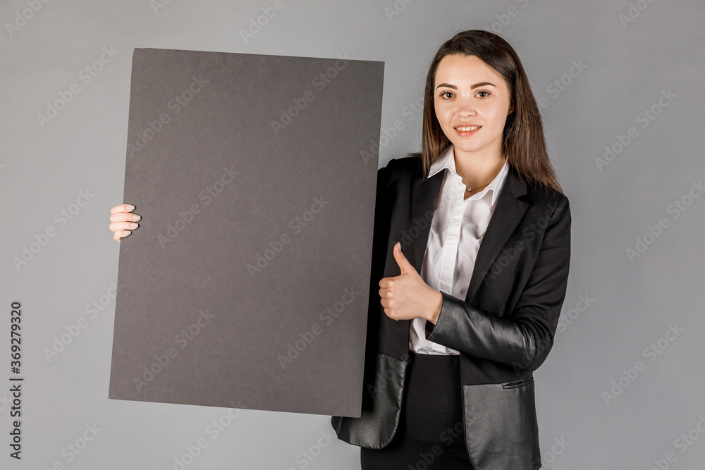 Young business woman in dark suite with black board on grey background. Young business woman in dark suite with black board on grey background.
