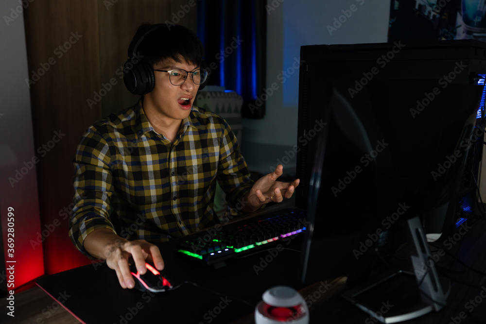 Asian man gamer in headphones stressed with hand feel depressed or angry shocked when losing the video game on computer Fear and upset for mistake, video game technology and e-sport concept - obrazy, fototapety, plakaty 