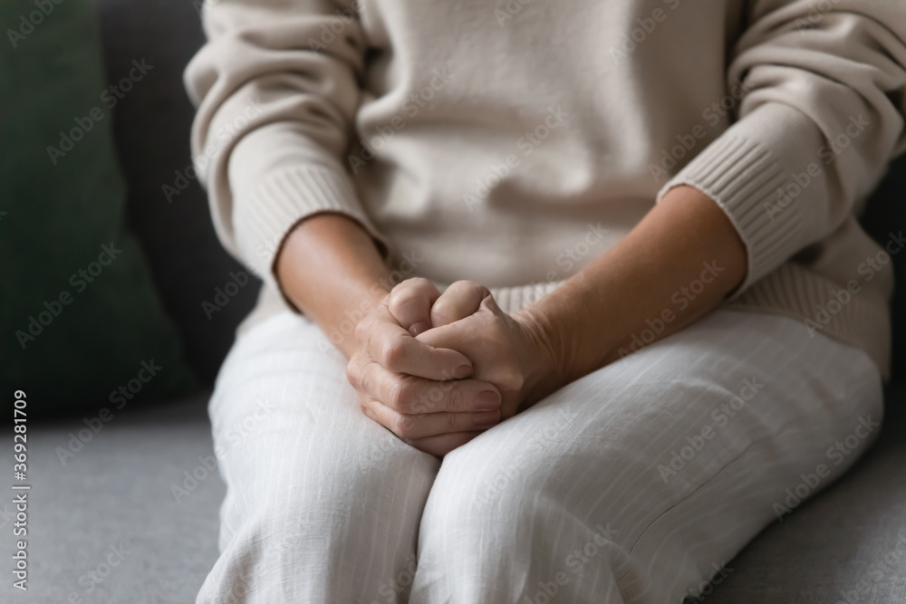 Close up image elderly woman feels nervous anxious or lonely put clenched hands on laps sitting on couch indoors. Older patient of nursing home, senile diseases and geriatric, declining years concept Close up image elderly woman feels nervous anxious or lonely put clenched hands on laps sitting on couch indoors. Older patient of nursing home, senile diseases and geriatric, declining years concept