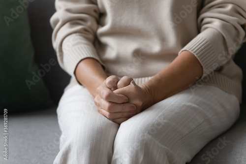 Bild auf Leinwand Close up image elderly woman feels nervous anxious or lonely put clenched hands on laps sitting on couch indoors