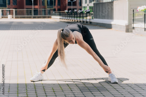 A girl in sportswear outdoors makes forward bends for stretching  trains the gluteal muscles for weight loss.