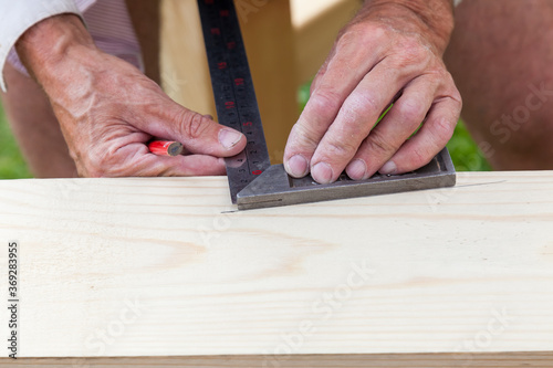 Close-up of the hands of an elderly craftsman - carpenter at work holding a metal ruler and a graphic pencil drawing markings on a wooden beam.