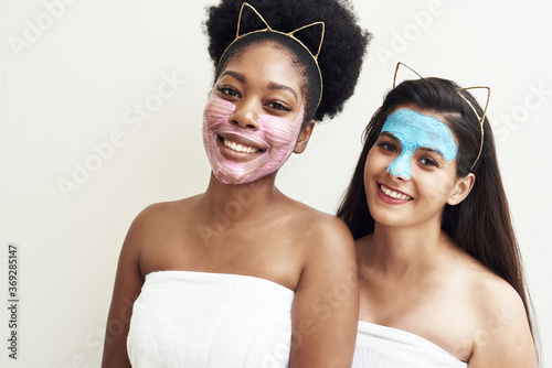 Multimasking. Two different ethnic girls are hugging. The girls' faces are covered with pink and blue face care masks. Beauty face, facial treatment and spa concept photo