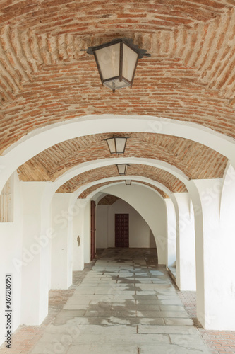a portico in a Spanish town  with a brick vault ceiling and old lamps