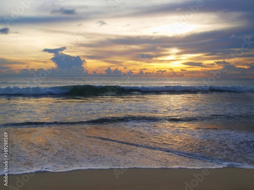 Fototapeta Naklejka Na Ścianę i Meble -  Seascape at sunset. Sundown abowe the sea. Cirrus clouds of unusial form on the dark sky on the evening. Glimpses of a bright orange sun. Reflection on a surface of water. Waves, beach, coast, ocean.