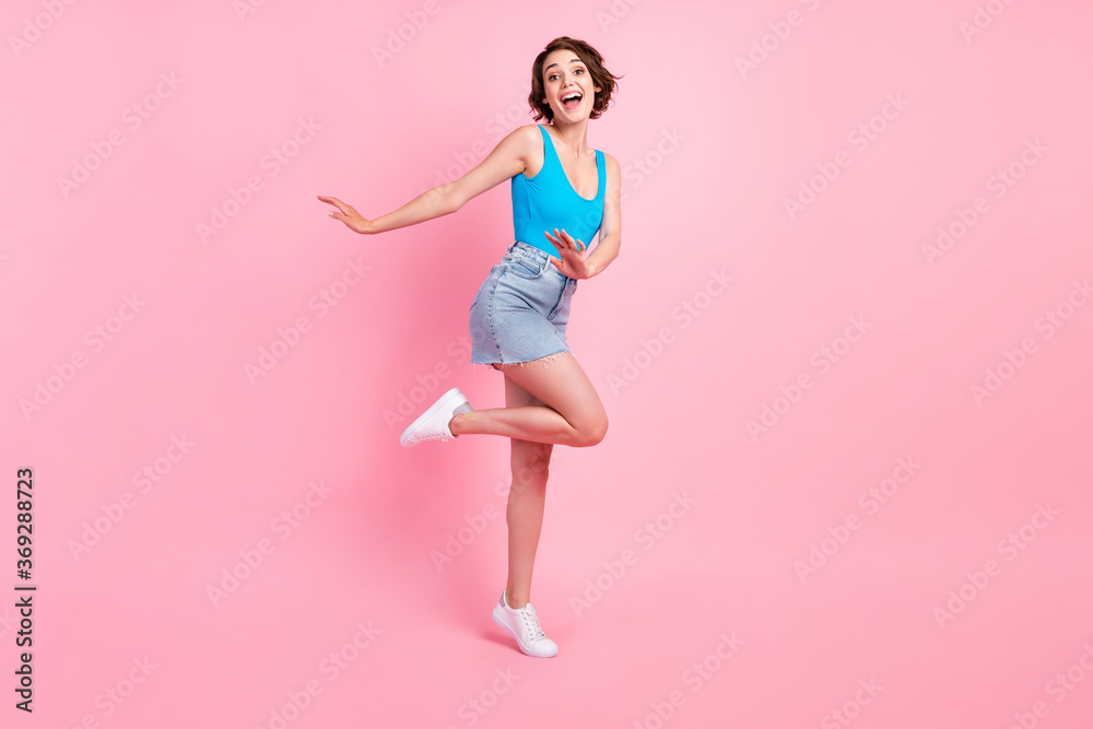 Full body size photo of pretty lovely young girl careless dancing smiling have fun open mouth weekend wear denim mini skirt blue singlet white sneakers isolated pink color background