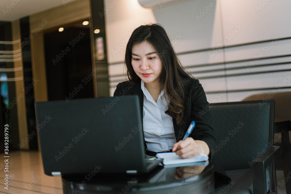 Beautiful young asian woman in suit using laptop and writing note Beautiful young asian woman in suit using laptop and writing note