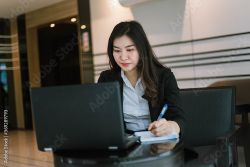 Beautiful young asian woman in suit using laptop and writing note © Near