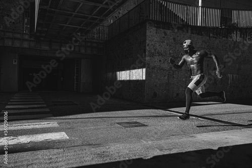 Athletic black man is training in front of the grey wall while wearing a mask. Black and white photo.