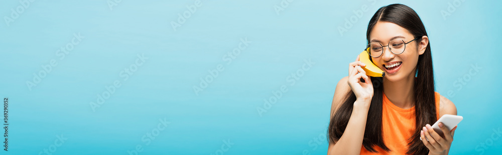 Φωτογραφία panoramic concept of happy asian girl in glasses holding smartphone and banana o