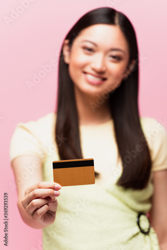 selective focus of happy asian woman holding credit card isolated on pink