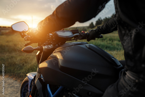 Close-up photo of biker sitting on motorcycle in sunset on the country road.