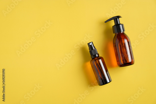 Dark amber glass bottles with natural cosmetics. Flat lay pump bottle with liquid soap and sprayer on yellow background.
