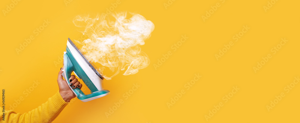 modern iron with steam in hand over yellow background, panoramic mock-up image