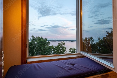 Beautiful summer sundown view from open window. Top of green trees on lake and cloudy sky background. 