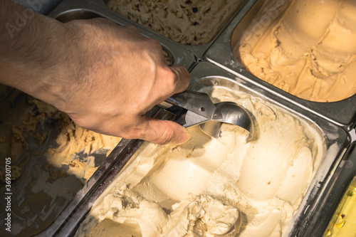 close up of a hand of a seller making vanilla ice cream scoop, hot summer weather refreshment snack
