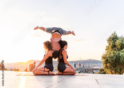 Beautiful man and two women doing acroyoga in the city. Harmony and relaxation with urban view
