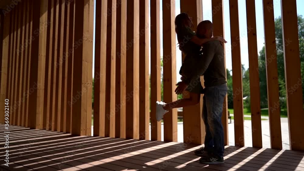 A slender girl in a dress and white sneakers runs and jumps into the arms of her bald brutal man. A loving couple are in the open air against a wooden fence. A slender girl in a dress and white sneakers runs and jumps into the arms of her bald brutal man. A loving couple are in the open air against a wooden fence.