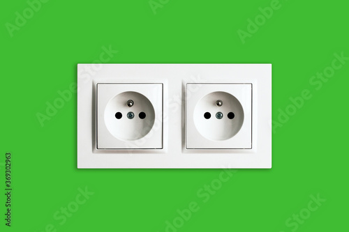 Brand new electrical socket isolated on green wall. Renovated studio apartment power supply background. Empty copy space double white plastic power outlet. Be eco and save energy.