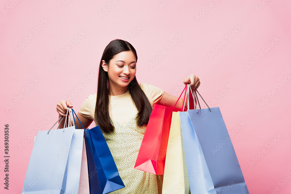 cheerful young asian woman looking at shopping bags isolated on pink cheerful young asian woman looking at shopping bags isolated on pink
